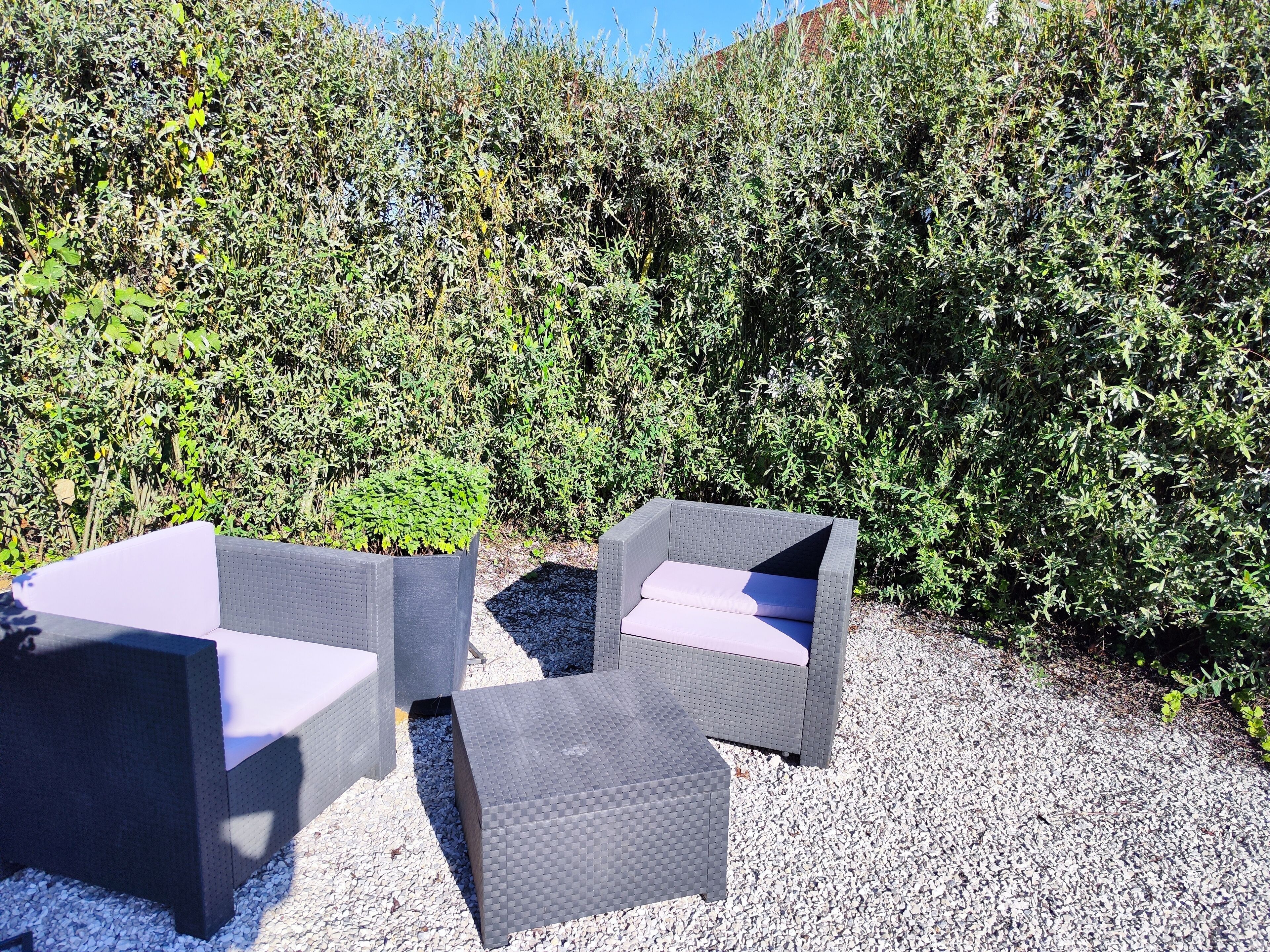 Deux fauteuils en osier pour l’extérieur, dotés de coussins, placés sur une surface de gravier et entourés d’une végétation luxuriante.