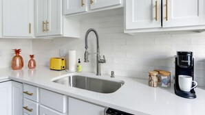A modern kitchen with white cabinets, a stainless steel sink, a yellow toaster, and a coffee maker. - Heritage Loft @ The Murphy House, Chippewa Square! (Savannah)