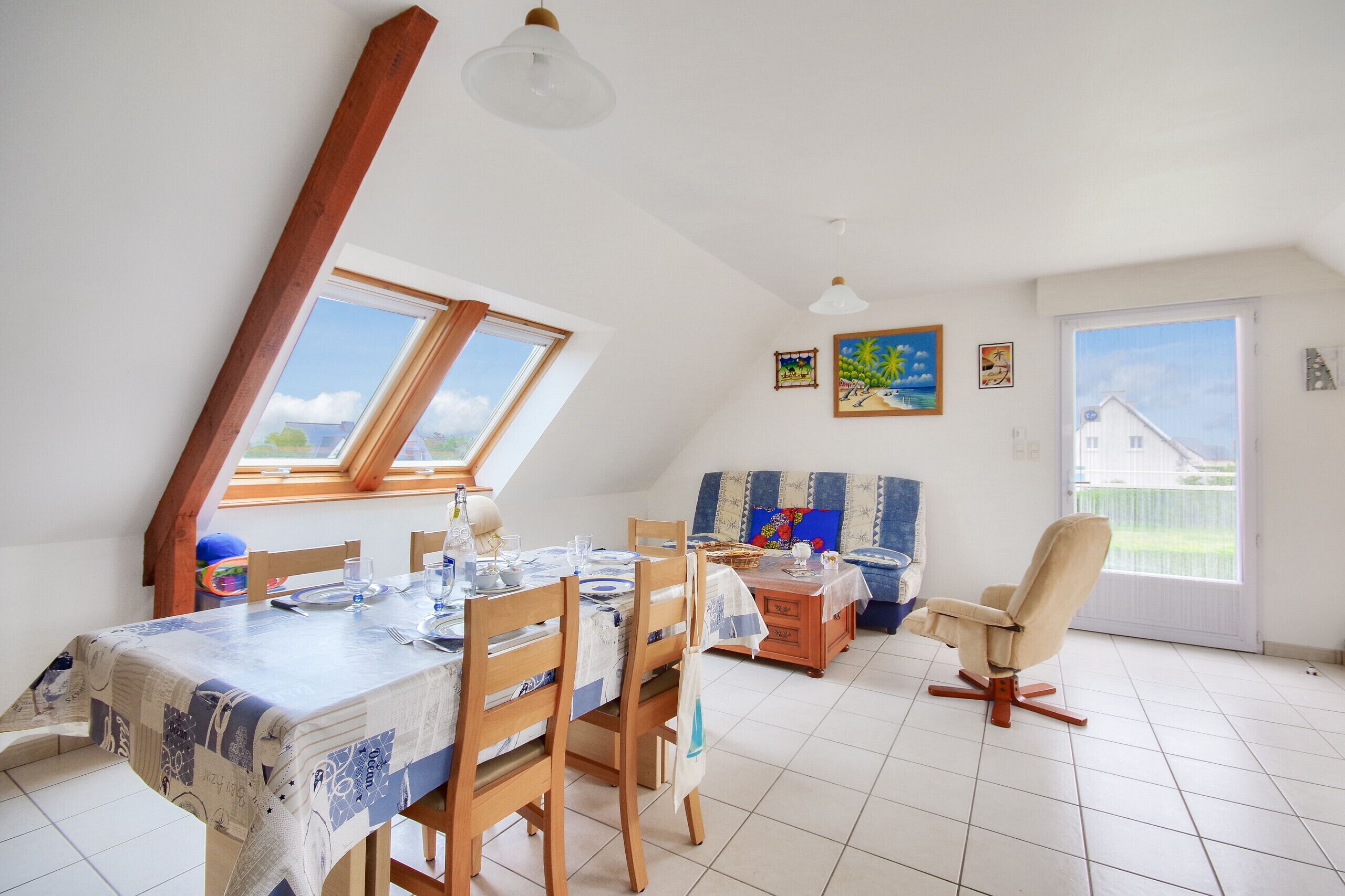 A dining area with a table set for four, wooden chairs, a wooden cabinet, and a window with a view of greenery.