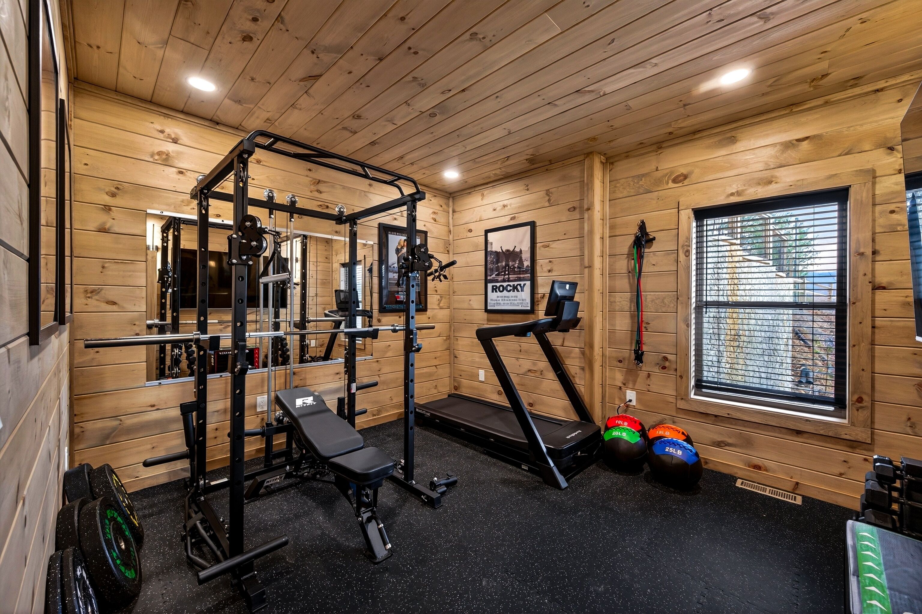 Une salle de sport avec des murs en bois, un banc, un tapis de course et du matériel d’haltérophilie.