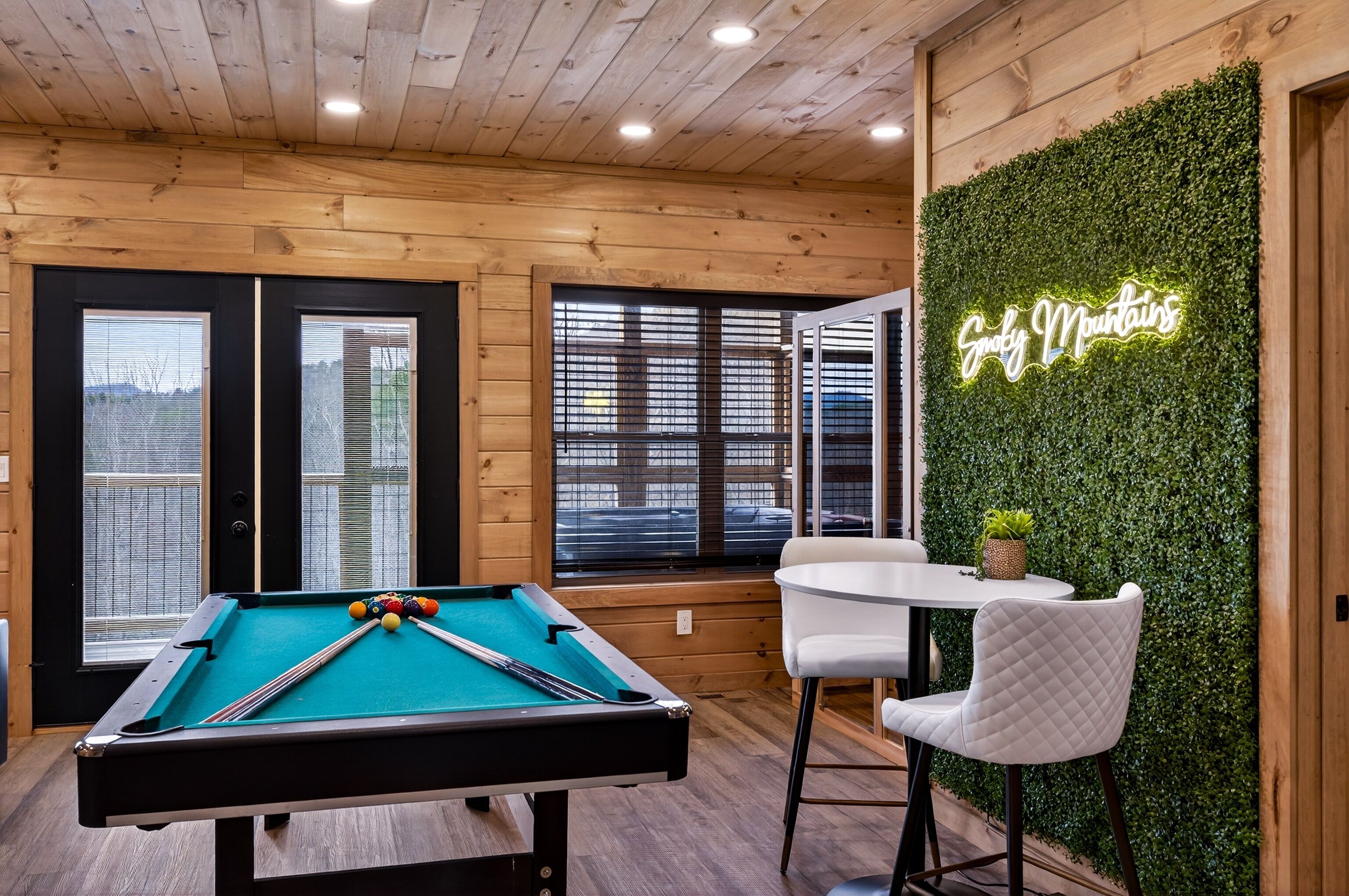 Une table de billard avec un néon, des murs en bois et un mur vert orné d’une plante.