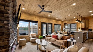 A spacious living area with a stone wall, wooden ceiling, and large windows.