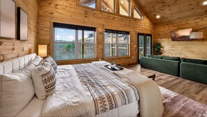 A spacious bedroom with a large bed, a green sofa, and multiple windows offering a view of the outdoors.