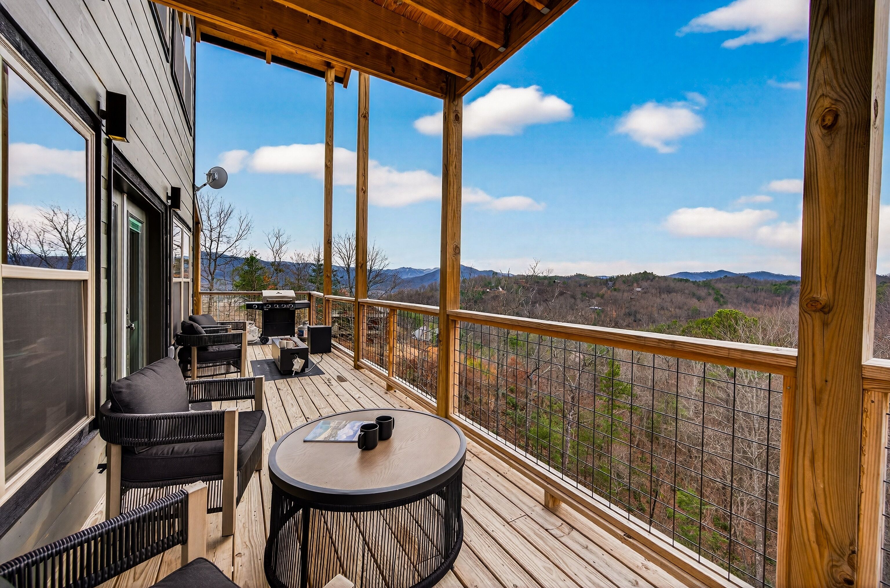 A wooden deck with outdoor furniture, a table, and a scenic view of mountains and trees.