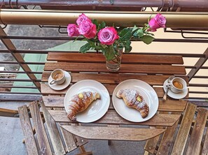 A wooden table with two plates of pastries and two cups of coffee, a vase with pink roses, and a metal railing in the background. - Apartment with balcony 5 min from the Vatican Museums and 3 min from the metro (Roma)
