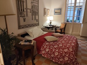 A hotel room with a bed, a desk, a chair, a lamp, and a large window. - Apartment with balcony 5 min from the Vatican Museums and 3 min from the metro (Roma)