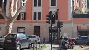 Um edifício de vários andares com varandas, área de estacionamento e rua com carros e semáforo.
