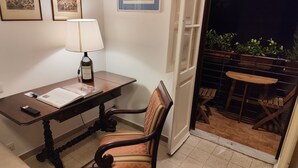 Um espaço de estudo com escrivaninha, cadeira, luminária e uma garrafa de vinho.