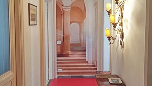 Um corredor com carpete vermelho, tapete estampado, escada com arcos e luminária fixada na parede.