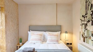 Ein ordentlich eingerichtetes Schlafzimmer mit Bett, Kissen, einer Nachttischlampe und einem Wandbild.