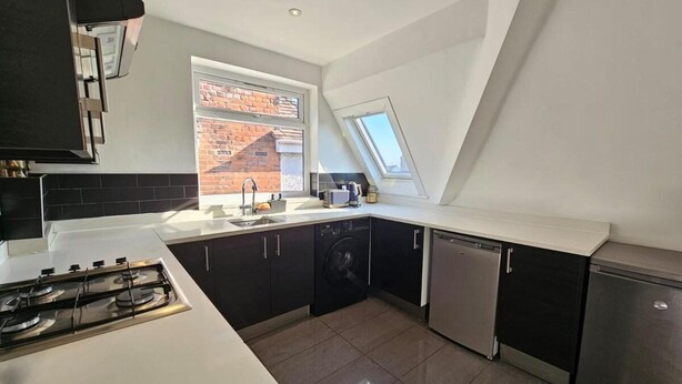 A modern kitchen with a gas stove, black cabinets, a dishwasher, and a window with a view of a brick building. - Apartment - Sleeps 4 & Free Parking (London)
