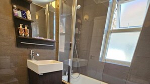 A modern bathroom with a glass-enclosed shower, a white sink, and a shelf with toiletries. - Apartment - Sleeps 4 & Free Parking (London)