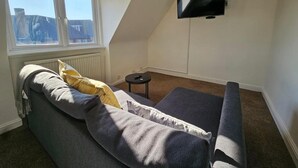 A cozy room with a grey sofa, a small black table, and a TV mounted on the wall. - Apartment - Sleeps 4 & Free Parking (London)