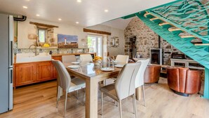 A spacious kitchen with a dining area, stone walls, and a rustic fireplace. - Longère Charmante et Confortable, Proche de la Pointe Saint Mathieu (Plougonvelin)