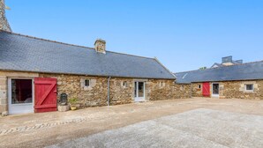A stone building with a tiled roof, a gravel driveway, and a red door. - Longère Charmante et Confortable, Proche de la Pointe Saint Mathieu (Plougonvelin)