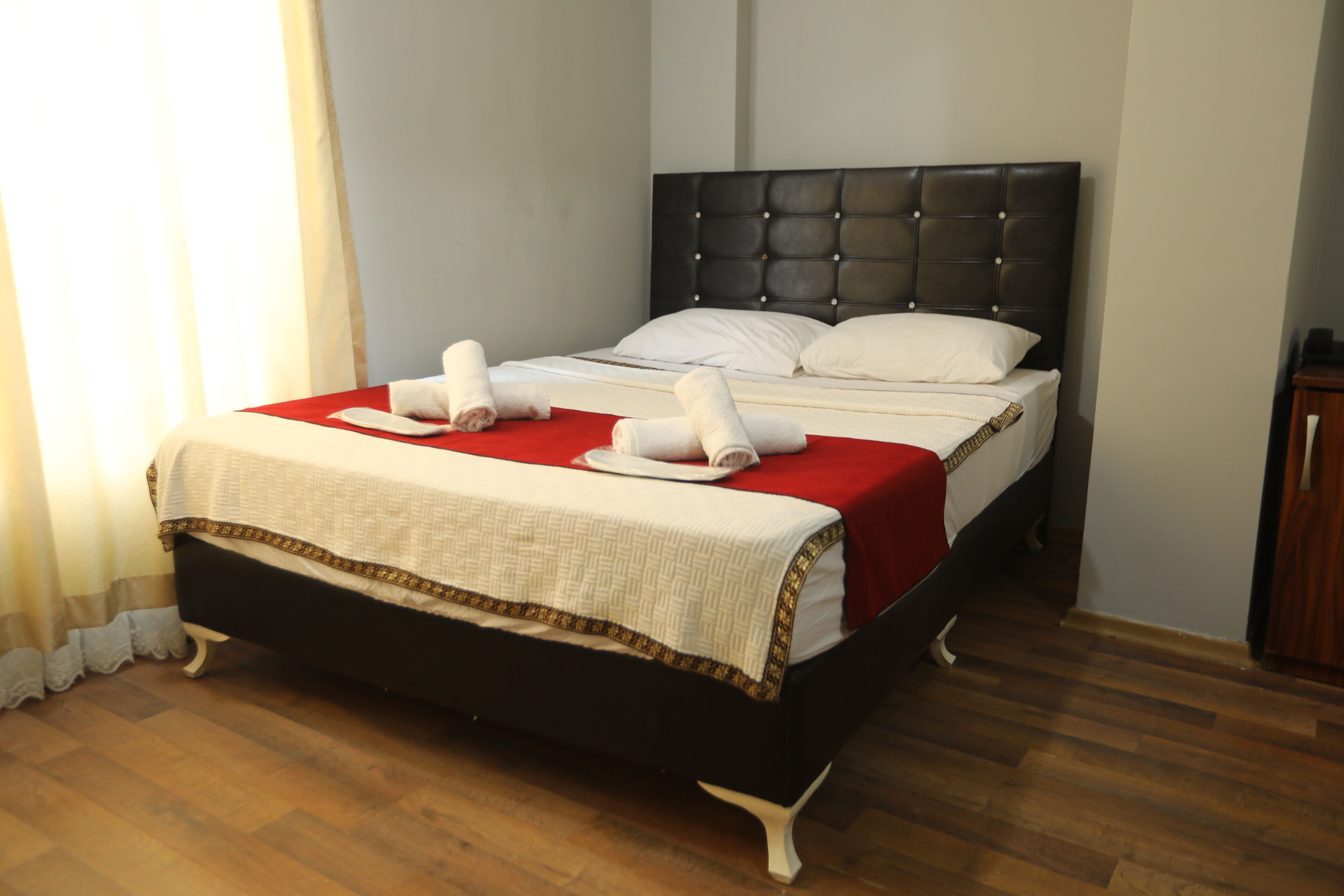 Ein ordentlich gemachtes Bett mit einer roten und weißen Bettdecke, einem schwarzen Kopfteil und zwei aufgerollten Handtüchern auf dem Bett.