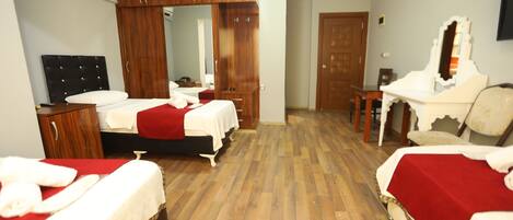 A hotel room with two beds, wooden flooring, a wardrobe, a mirror, and a desk.