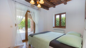 Un dormitorio con cama, suelo de madera, paredes blancas, una ventana y una puerta que da a un espacio exterior.