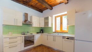 Cocina con gabinetes blancos, horno de acero inoxidable, lavavajillas y ventana con vistas a follaje.