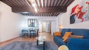 A living room with a blue sofa, a glass coffee table, and a dining area with chairs and a table. - Charming townhouse with a covered and furnished interior patio (Tournus)