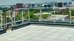 Terraza en la azotea con vistas a la ciudad, con edificios modernos y un cielo nublado.