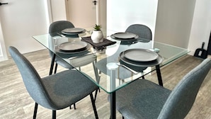 Un comedor moderno con una mesa de vidrio, sillas tapizadas grises y una pequeña planta en maceta.