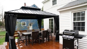 Un patio exterior con zona de estar cubierta, una parrilla y una mesa de comedor con sillas.