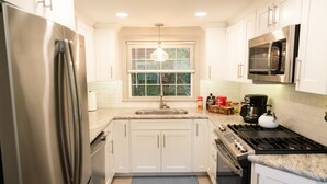 Una cocina moderna con armarios blancos, electrodomésticos de acero inoxidable, encimera de granito y ventana con persianas.