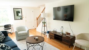 Una sala de estar con sofá, sillón, mesa de centro, televisor y escalera.