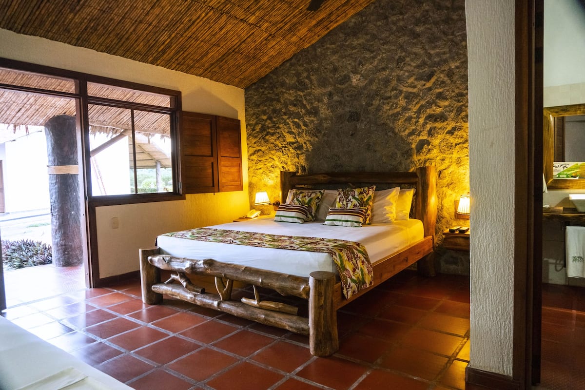Ein rustikales Schlafzimmer mit Steinwand, Holzbettgestell und Fliesenboden.