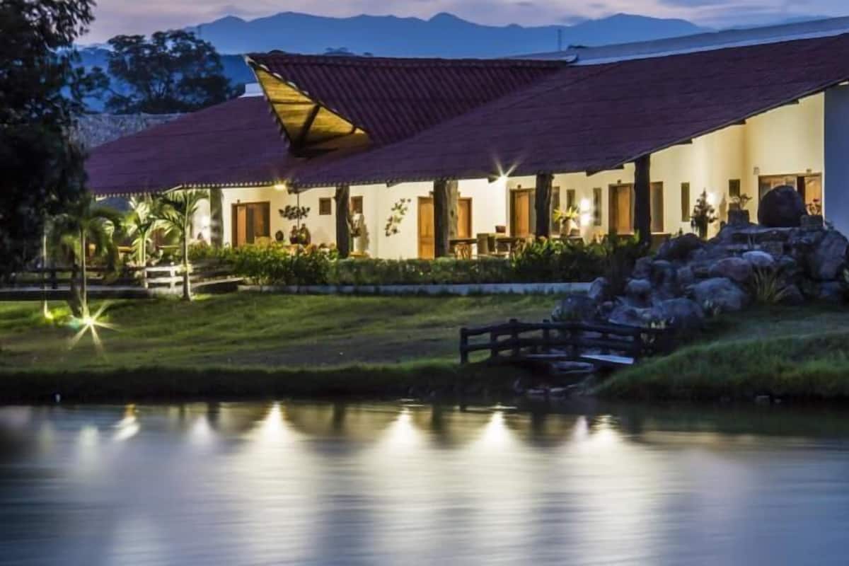 Ein Hotel mit einer großen Terrasse, einem Teich und einer Bergkulisse.