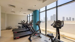 A gym with treadmills and elliptical machines, large windows with a city view, and a teal-colored pillar.