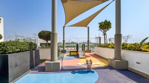 An outdoor play area with colorful flooring, seating, and shade structures.