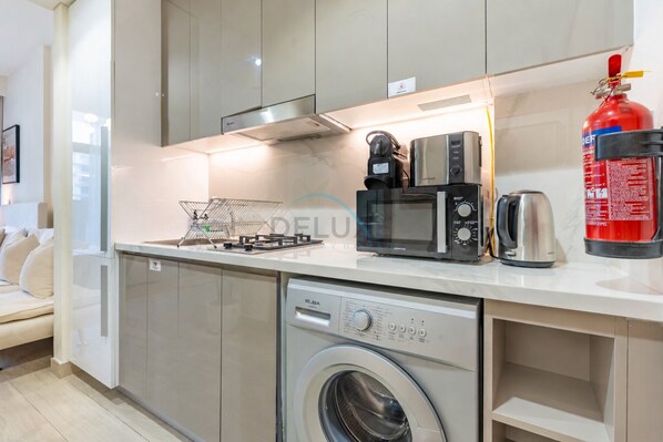 A modern kitchen with a built-in washer, a gas stove, a coffee maker, and a fire extinguisher.