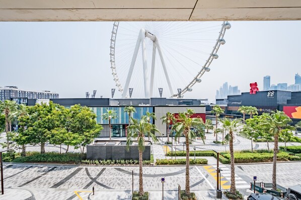 Una plaza urbana moderna con una noria gigante, palmeras y edificios contemporáneos.