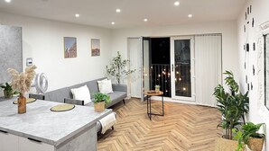 Een moderne woonkamer met een grijze bank, een eettafel met placemats, en een visgraatparketvloer.