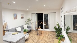 Een moderne woonkamer met een grijze bank, een eettafel en een visgraatparketvloer.