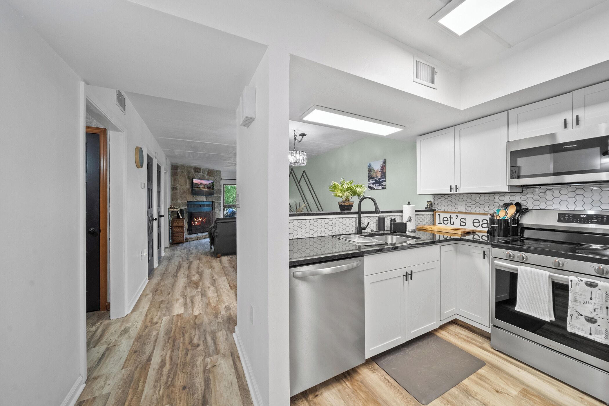 A modern kitchen with white cabinets, stainless steel appliances, and a wooden floor.