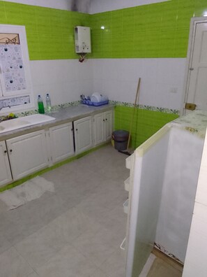 A kitchen with white cabinets, a sink, a green-tiled backsplash, and a white refrigerator.