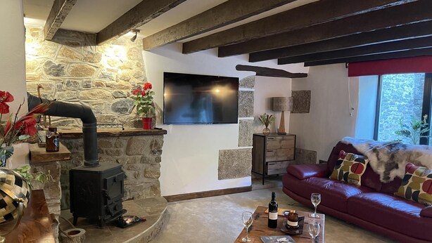 Una sala de estar acogedora con pared de piedra, chimenea, sofá de cuero y mesa de centro de madera con copas de vino.