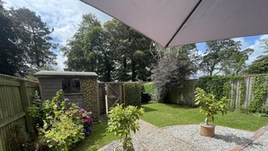 Un patio trasero con un cobertizo de madera, un camino de grava y una pequeña zona de césped.