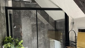 Un baño moderno con cabina de ducha de vidrio, un lavabo con una planta y un estante pequeño con un gancho.