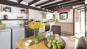 Una cocina con armarios blancos, una mesa de madera, un jarrón de flores y un cuenco de manzanas.