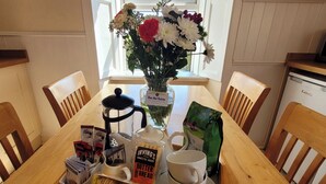 Une table de salle à manger en bois, agrémentée d’un arrangement floral, d’une cafetière, d’une tasse, d’un sachet de beurre et d’un plateau contenant des biscuits et une boîte de thé.