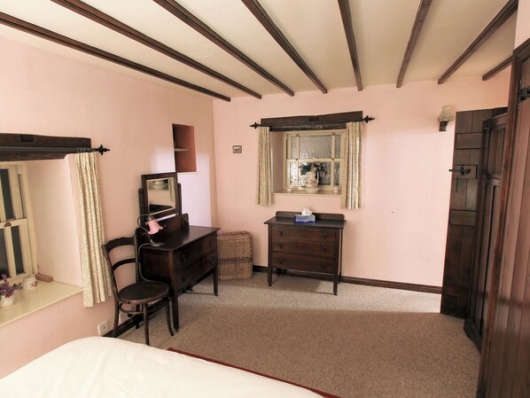 A bedroom with a bed, a dresser, a chair, a desk with a mirror, and a window with curtains.
