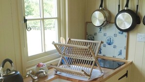 A kitchen with a wooden drying rack, a kettle, and two hanging pans. - Beeches Shepherd Hut (Harleston)