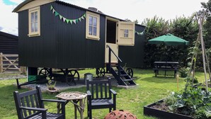 A rustic wooden building with a small porch, outdoor seating, and a decorative metal sphere. - Beeches Shepherd Hut (Harleston)