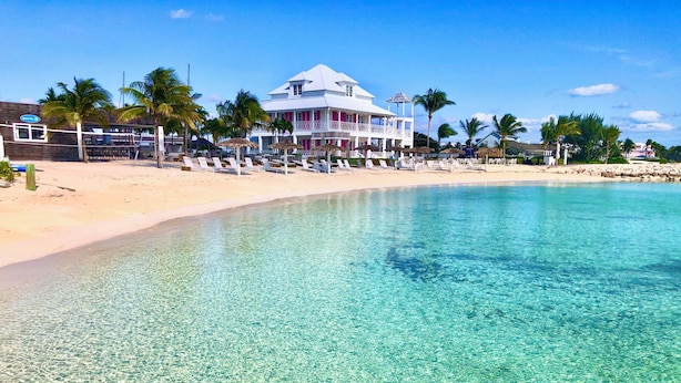 A beachfront hotel with clear blue water, palm trees, and a sandy beach.