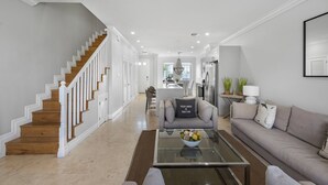 A modern living room with a staircase, a dining area, and a kitchen.
