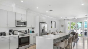 A modern kitchen with stainless steel appliances, a central island with bar stools, and a view to the outside.